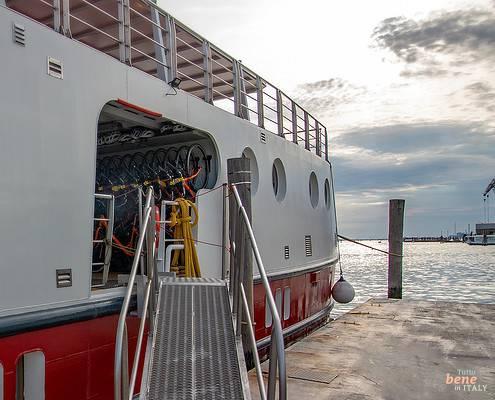 View of the gangway and the open bicycle storage on the hotel barge Ave Maria in the Venice Lagoon under a cloudy sky.