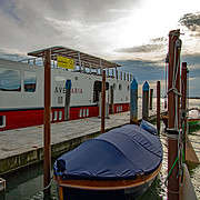 The white and red hotel barge "Ave Maria" for Bike & Barge tours moored at a pier in the Venice Lagoon, with a covered boat in the foreground.