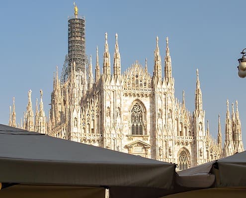 Atmospheric Milan Cathedral – Gothic Splendor • m24o Moody view of the Milan Cathedral (Duomo di Milano) featuring wet cobblestones reflecting the Gothic facade, with passersby under umbrellas.