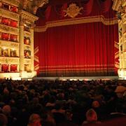 View of the occupied auditorium of the Teatro alla Scala in Milan with the magnificent red stage curtain before an opera performance.