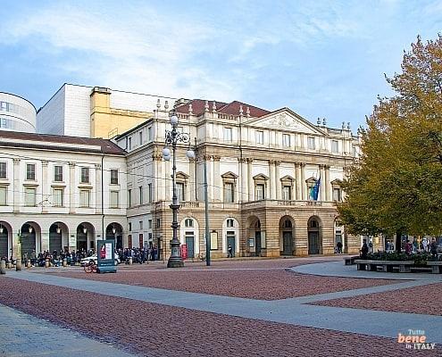 Willkommen im Teatro alla Scala – Ihr Opernerlebnis in Mailand • m24o Die neoklassizistische Fassade des Teatro alla Scala in Mailand mit herbstlich gefärbten Bäumen auf der Piazza della Scala und dem modernen Bühnenturm im Hintergrund.