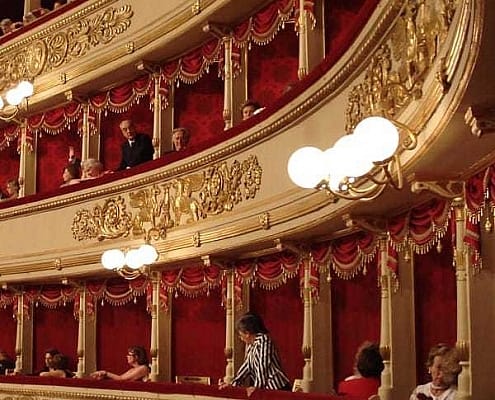The historic gold-decorated boxes at Teatro alla Scala in Milan with red velvet lining and opera guests; Photo © Amro - stock.adobe.com