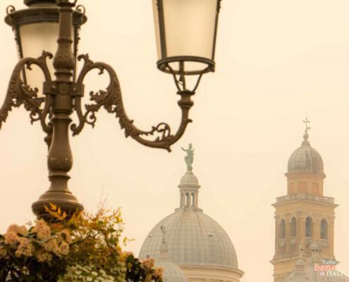 A historic street lamp with flower boxes in the foreground, with the domes of the Basilica of Santa Giustina in the background.