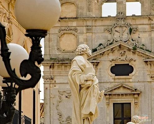 Statue of Saint Lucia, in the background the Church of Santa Lucia al Sepolcro with the "Burial of Saint Lucia"