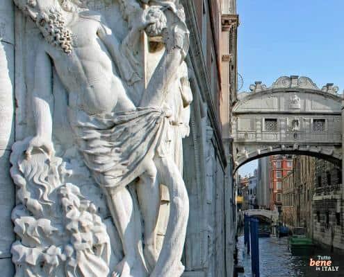 Venedigs Geschichte entdecken: Seufzerbrücke und Dogenpalast • m24o Detailreiche Skulptur eines bärtigen Mannes (Noah) am Dogenpalast in Venedig mit Blick auf die Seufzerbrücke über einem Kanal.