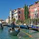 Gondoliers steering their gondolas on the sunny Grand Canal in Venice past historic Venetian palaces.