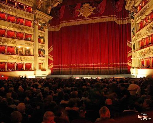 Der Saal der Scala in rotem Samt • m24o Der festlich beleuchtete Zuschauerraum des Teatro alla Scala in Mailand mit dem ikonischen roten Vorhang und erwartungsvollem Publikum.