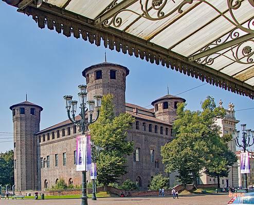 Palazzo Madama mittelalterliche Festung in Turin • m24o Blick auf die mittelalterliche Backsteinfassade des Palazzo Madama in Turin mit Wehrtürmen unter blauem Himmel, fotografiert unter dem verzierten Glasdach des historischen Pavillons der Piazza Castello.