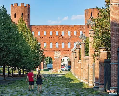 Porta Palatina Turin Roman City Gate Ancient Ruin Brickwork • m24o A couple walks down a path lined with trees and brick pillars towards the ancient Roman gate Porta Palatina in Turin.