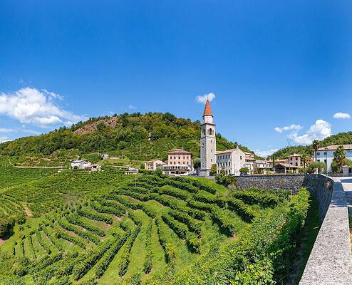 Steep vineyards of the Prosecco region near Valdobbiadene in Veneto under a bright blue sky.