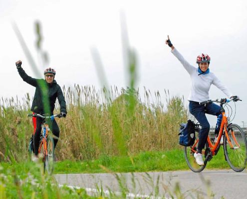 A happy couple enjoying a cycling tour through Italy from Mantua to Venice, waving joyfully at the camera; Photo © Girolibero.