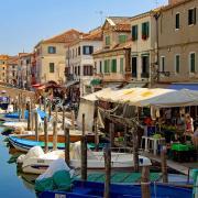 The picturesque Canal Vena in Chioggia near Venice with colorful fishing boats, market stalls along the bank, and historic houses.