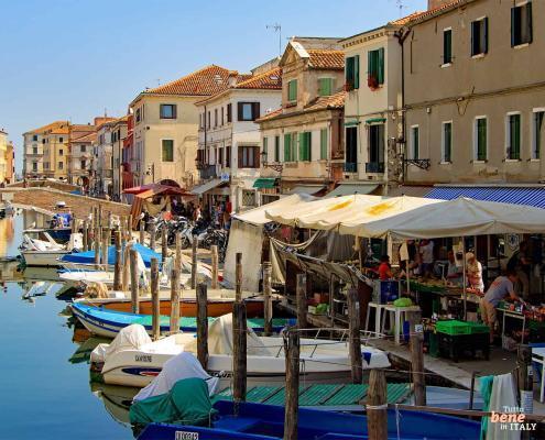 The picturesque Canal Vena in Chioggia near Venice with colorful fishing boats, market stalls along the bank, and historic houses.