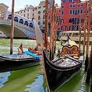 Classic view of the white Rialto Bridge over the Grand Canal in Venice featuring two elegant gondolas in the foreground.