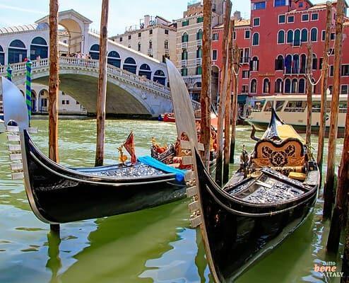 Klassischer Blick auf die weiße Rialtobrücke über den Canal Grande in Venedig mit zwei eleganten Gondeln im Vordergrund.
