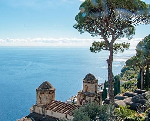 Historic towers of Villa Rufolo in Ravello with the iconic stone pine tree and a panoramic view of the blue Mediterranean Sea.