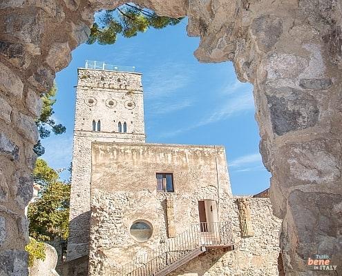 The imposing Torre Maggiore of Villa Rufolo in Ravello, framed by a historic stone archway under a clear blue sky.