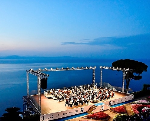 Panoramic view of the Ravello Festival: Orchestra on the Villa Rufolo Belvedere stage during the blue hour overlooking the Gulf of Salerno.