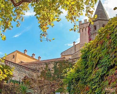 View of the medieval architecture and towers of Villa Cimbrone in Ravello, framed by autumn leaves and lush greenery.