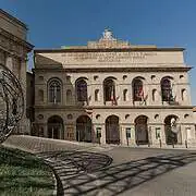 Exterior view of the Sferisterio in Macerata, a monumental historic open-air theatre in the Marche region, which serves as the main stage of the Macerata Opera Festival. The long façade with its round-arched arcades and neoclassical architecture dominates the square and reflects its original use as a sports arena as well as its current importance as an opera venue.