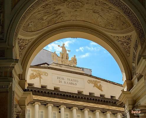 View of the Teatro di San Carlo from the Galleria Umberto I • m24o The "Real Teatro di S. Carlo" inscription on the opera house facade in Naples, framed by the ornate arches of Galleria Umberto I under a blue sky.