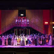 Teatro Regio Torino Opera La Rondine Stage Design Ensemble • Teatro Regio Turin: Foto Andrea Macchia Cast and choir in elegant costumes on a vibrant red lit opera stage at Teatro Regio di Torino with falling confetti.