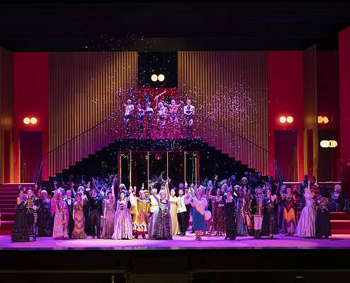 Teatro Regio Torino Opera La Rondine Stage Design Ensemble • Teatro Regio Turin: Foto Andrea Macchia Cast and choir in elegant costumes on a vibrant red lit opera stage at Teatro Regio di Torino with falling confetti.