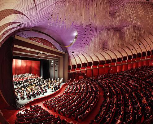 Teatro Regio Torino Opera Interior Stage • Foto Edoardo Piva Wide view of the stage with orchestra and choir inside the packed auditorium of Teatro Regio di Torino featuring its modern purple ceiling.