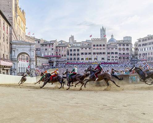 Horse racing event at a historic city square with a large crowd and colorful buildings in the background. • Fotostudio Donati Palio di Siena, das Festival in der Piazza del Campo