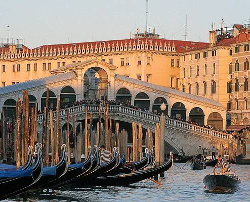 The historic Rialto Bridge in Venice bathed in the warm light of the winter evening sun, with gondolas moored in the foreground.