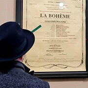Opera Night at La Scala – La Bohème • m24o A man in a hat studying the official opera poster for La Bohème by Giacomo Puccini at Teatro alla Scala.