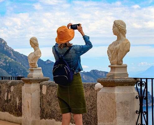 Terrace of Infinity at Villa Cimbrone, Ravello • m24o A tourist wearing an orange hat takes a photo of the Amalfi Coast from the famous "Terrace of Infinity" in Ravello. Classical marble busts on a stone wall frame the panoramic view of the Mediterranean Sea.