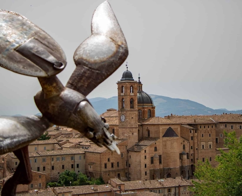 View of the Ducal Palace in Urbino with Sculpture • m24o View over a modern metal sculpture in the foreground towards the historic skyline of Urbino, featuring the Palazzo Ducale and the Cathedral.