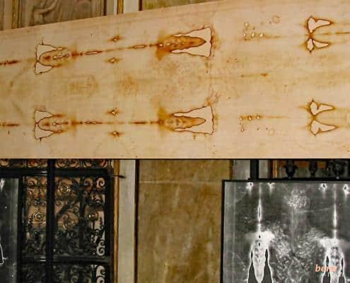 The Shroud of Turin at the Cathedral of Saint John the Baptist • m24o An exhibition of the Shroud of Turin showing the original light-colored linen cloth with burn marks and body imprints above, and two large photographic negative enlargements of the face and torso below.