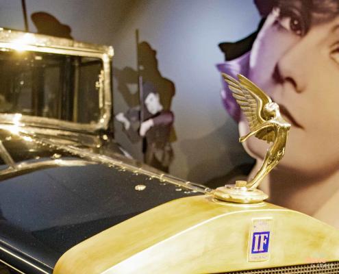 Isotta Fraschini vintage car at MAUTO Automobile Museum in Turin • m24o The golden winged hood ornament and blue IF logo of a historic Isotta Fraschini 8A at the Turin Automobile Museum (MAUTO), with a large black-and-white portrait of actress Gloria Swanson in the background.