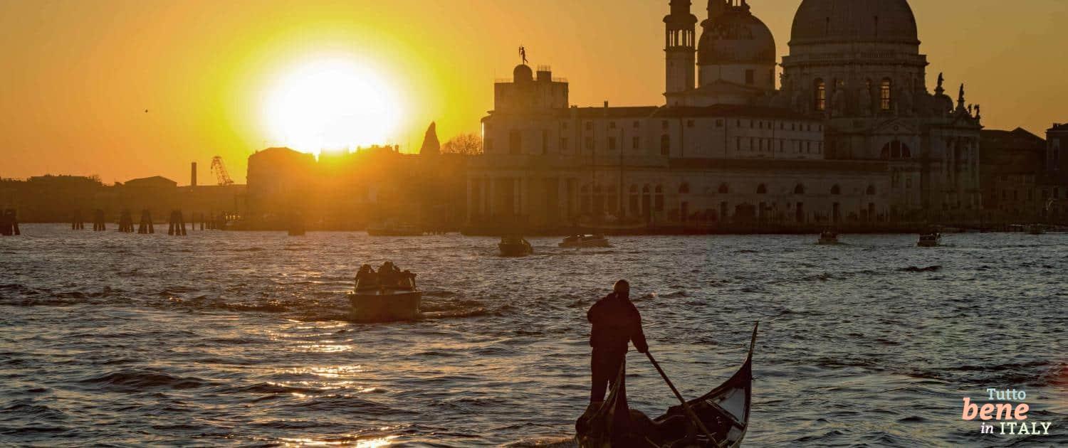 Silhouette of a gondolier on his gondola in the Grand Canal during a low, golden winter sunset in front of the Santa Maria della Salute Basilica.