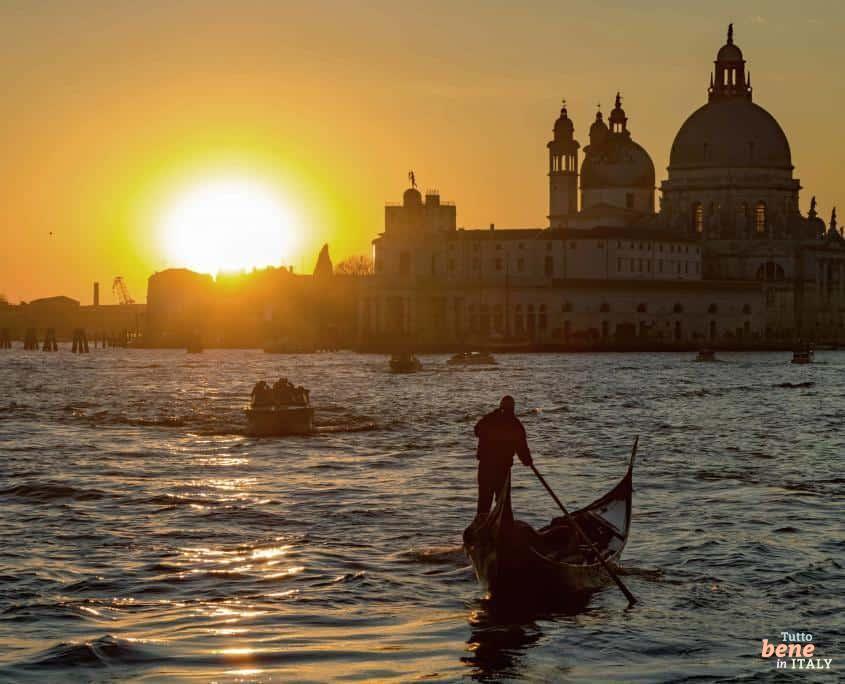 Eine Gondel auf dem Canal Grande in Venedig bei Sonnenuntergang mit der Basilika Santa Maria della Salute im Hintergrund.