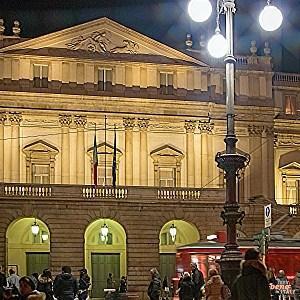 Vorfreude am Abend: Die Mailänder Scala erwartet ihr Publikum Das nachts beleuchtete Teatro alla Scala in Mailand mit Fußgängern auf der Piazza und einer vorbeifahrenden roten Straßenbahn im Vordergrund.