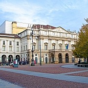 Welcome to Teatro alla Scala – Your Opera Experience in Milan • m24o The neoclassical facade of Teatro alla Scala in Milan with autumn trees at Piazza della Scala and the modern stage tower in the background.