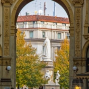 Ein Fenster zur Kunst: Von der Galleria zum Denkmal Leonardos • m24o Blick durch das prächtige Portal der Galleria Vittorio Emanuele II auf das Leonardo-da-Vinci-Denkmal und die herbstliche Piazza della Scala in Mailand.