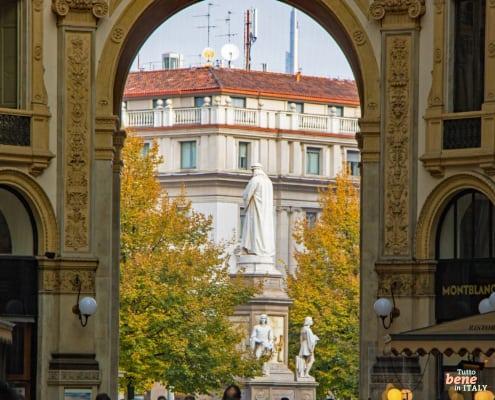 Ein Fenster zur Kunst: Von der Galleria zum Denkmal Leonardos • m24o Blick durch das prächtige Portal der Galleria Vittorio Emanuele II auf das Leonardo-da-Vinci-Denkmal und die herbstliche Piazza della Scala in Mailand.