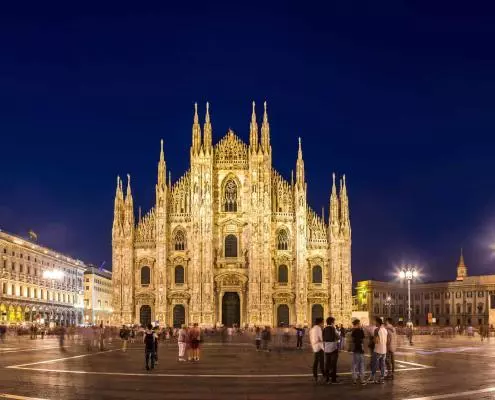 Milan Cathedral at night with people relaxing in the cathedral square.