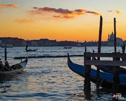 Pure Romance: Gondola Ride in Venice at Sunset • m24o A gondolier steering his gondola on the Grand Canal in Venice during a vibrant orange sunset, with the city's silhouette in the background.