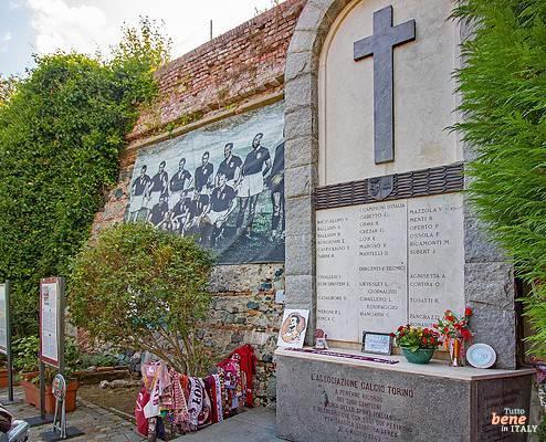 Grande Torino Gedenkstätte bei der Basilica di Superga in Turin • m24o Die steinerne Gedenktafel für die verunglückte Fußballmannschaft Grande Torino an einer Backsteinmauer in Superga mit einem historischen Mannschaftsfoto links, einem Steinkreuz oben, gravierten Namen und abgelegten Fan-Schals und Blumen im Vordergrund.