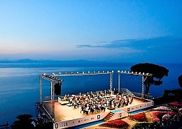 Ravello Festival Panorama – Konzert über dem Meer • Ravello Festival | ph Vincent Ruocco Panoramablick auf das Ravello Festival: Orchester auf der Bühne des Villa Rufolo Belvedere während der blauen Stunde mit Blick auf den Golf von Salerno.