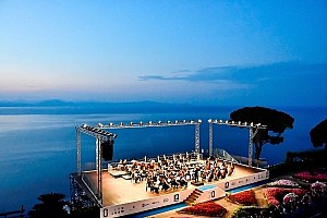 Ravello Festival Panorama – Konzert über dem Meer • Ravello Festival | ph Vincent Ruocco Panoramablick auf das Ravello Festival: Orchester auf der Bühne des Villa Rufolo Belvedere während der blauen Stunde mit Blick auf den Golf von Salerno.