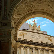 Blick auf das Teatro di San Carlo von der Galleria Umberto I • m24o Die Inschrift „Real Teatro di S. Carlo“ an der Fassade des Opernhauses in Neapel, eingerahmt von den kunstvollen Bögen der Galleria Umberto I unter blauem Himmel.