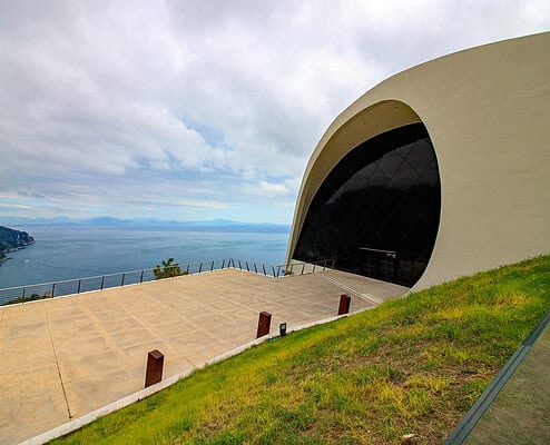 Die markante wei&szlig;e, geschwungene Architektur des Oscar Niemeyer Auditoriums in Ravello vor der Kulisse des blauen Mittelmeers und der Amalfik&uuml;ste unter bew&ouml;lktem Himmel.