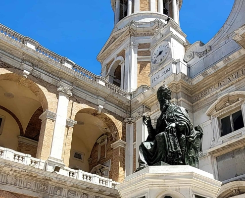 Monument to Pope Sixtus V, Loreto • m24o Bronze statue of Pope Sixtus V situated in front of the Apostolic Palace and the grand bell tower in Loreto, Italy, set against a clear blue sky.
