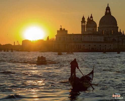 Winter Magic in Venice: Gondola Ride at the Turn of the Year • m24o Silhouette of a gondolier on his gondola in the Grand Canal during a low, golden winter sunset in front of the Santa Maria della Salute Basilica.